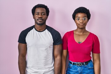 Sticker - Young african american couple standing over pink background relaxed with serious expression on face. simple and natural looking at the camera.