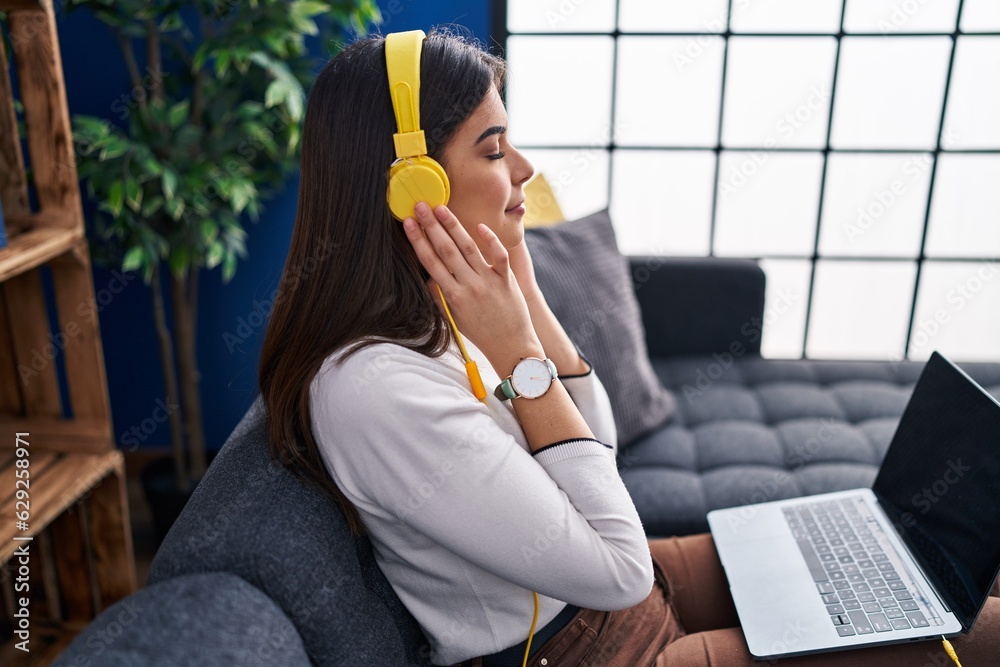 Young beautiful hispanic woman listening to music sitting on sofa at home