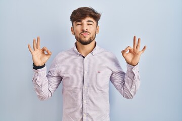 Canvas Print - Arab man with beard standing over blue background relaxed and smiling with eyes closed doing meditation gesture with fingers. yoga concept.