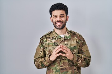 Wall Mural - Arab man wearing camouflage army uniform hands together and fingers crossed smiling relaxed and cheerful. success and optimistic