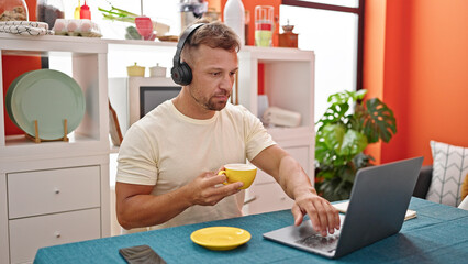 Poster - Young man using laptop and headphones drinking coffee at dinning room