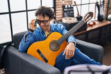 Poster - Young hispanic man musician playing classical guitar talking on smartphone at music studio