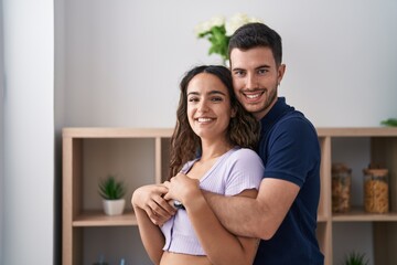 Wall Mural - Young hispanic couple hugging each other standing at home