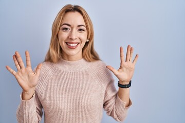 Canvas Print - Hispanic woman standing over blue background showing and pointing up with fingers number ten while smiling confident and happy.