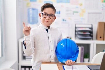 Sticker - Young hispanic kid holding architect hardhat at the office smiling happy pointing with hand and finger to the side