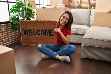 Canvas Print - Young hispanic woman holding welcome doormat at new home smiling and laughing hard out loud because funny crazy joke.