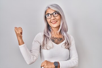 Sticker - Middle age woman with grey hair standing over white background smiling with happy face looking and pointing to the side with thumb up.