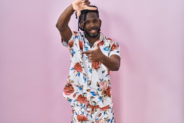 Poster - African man with dreadlocks wearing summer shirt over pink background smiling making frame with hands and fingers with happy face. creativity and photography concept.