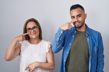 Sticker - Hispanic mother and son standing together pointing with hand finger to face and nose, smiling cheerful. beauty concept