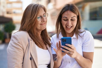 Sticker - Mother and daughter using smartphone standing together at street