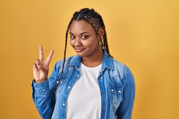 Poster - African american woman with braids standing over yellow background showing and pointing up with fingers number two while smiling confident and happy.