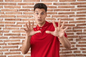 Wall Mural - Young hispanic man standing over bricks wall afraid and terrified with fear expression stop gesture with hands, shouting in shock. panic concept.