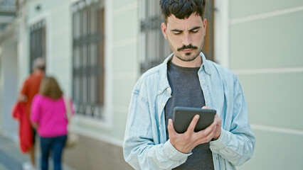 Sticker - Young hispanic man using touchpad with relaxed expression at street