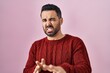 Young hispanic man with beard wearing casual sweater over pink background disgusted expression, displeased and fearful doing disgust face because aversion reaction. with hands raised