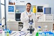 © Krakenimages.com - Young hispanic man with beard working at scientist laboratory amazed and smiling to the camera while presenting with hand and pointing with finger.