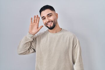 Sticker - Young handsome man standing over isolated background waiving saying hello happy and smiling, friendly welcome gesture