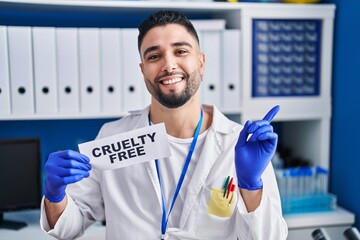 Wall Mural - Young handsome man working at scientist laboratory holding cruelty free banner smiling happy pointing with hand and finger to the side