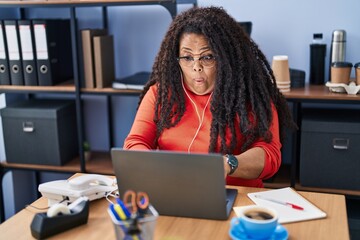 Sticker - Plus size hispanic woman working at the office with headphones scared and amazed with open mouth for surprise, disbelief face