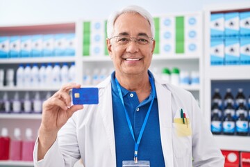 Sticker - Middle age man with grey hair working at pharmacy drugstore holding credit card looking positive and happy standing and smiling with a confident smile showing teeth