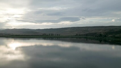 Poster - Landscape scene of brown hills and green land by reflecting river with sunset gray sky