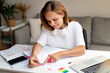 © Barillo Images - Girl student sitting at the desk at home and doing homework, sticking colourful bookmarks on page of her workbook.