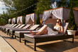 © artiemedvedev - Self employed woman telecommuting with team on project from tropical island resort. Freelancer businesswoman doing remote work with laptop on swimming pool beach bed at spa. Girl tanning and relaxing.