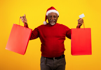 Wall Mural - Happy senior black man in Santa Claus hat holding credit card and Christmas gift bags with mockup for your brand logo