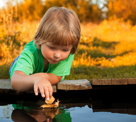 Wall Mural - boy play with autumn leaf ship in water