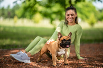 a girl plays with a french bulldog in the park on a jogging track