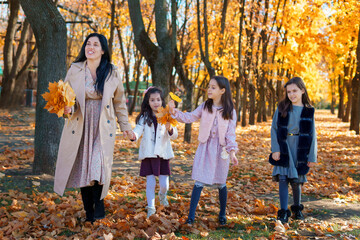 Wall Mural - mother and daughters are in autumn city park, happy people walking together, family with children, playing with yellow leaves, beautiful nature, bright sunny day