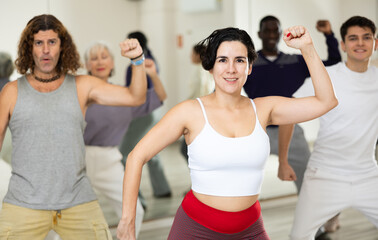 Wall Mural - Smiling young woman rehearsing modern dance with group in dance school