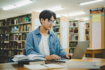 Male college students are working on laptops and searching for books to study, make reports, find useful information in college room. Concept of reading, learning and intelligence.