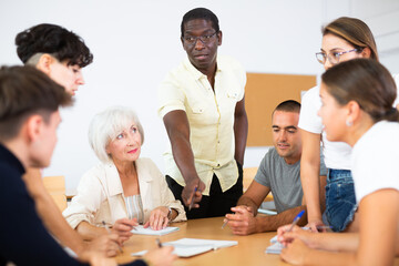 Wall Mural - Group of interested women and men of different ages and nationalities sitting around table and communicating