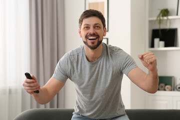 Wall Mural - Emotional man holding remote controller and watching TV at home