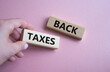 © Natallia - Back Taxes symbol. Concept word Back Taxes on wooden blocks. Businessman hand. Beautiful pink background. Business and Back Taxes concept. Copy space