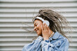 © Drobot Dean - Cheerful woman dancing while listening music with headphones outdoors near gray wall