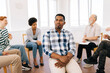 © dikushin - Portrait of sad African young man pensive looking away sitting in circle at group psychological counselling. Black male posing for picture treatment at therapy session. Concept of mental health