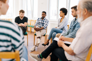 Back view to depressed black male drinker talking about alcohol addiction abuse sitting in circle speak to diverse addicted people at group therapy session. Concept of mental health, support.