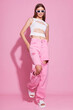 Young fashion woman in pink trendy jeans and white top on pink background.