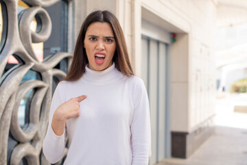 Wall Mural - pretty young adult woman looking shocked and surprised with mouth wide open, pointing to self