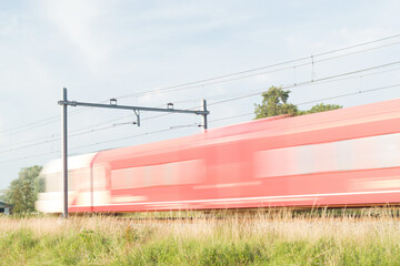 Wall Mural - Red and white train rushes by at high speed, blurred by long exposure in Arnhem in the Netherlands