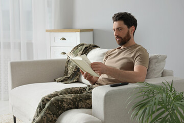 Wall Mural - Soldier reading book on soft sofa in living room. Military service