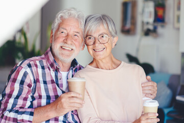 Sticker - Happy senior white-haired couple embracing at home enjoying a coffee cup. Forever love, elderly couple in love