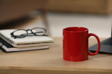 Canvas Print - Red ceramic mug, notebooks and laptop on wooden table at workplace. Space for text