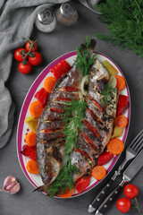 Seabass baked with vegetables served on a plate on a gray background, Top view