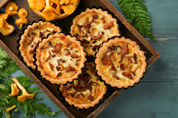 Savory hands pie with chanterelle mushrooms, cream and cheese on cutting board on rustic old wooden table background. Homemade tarts with seasonal chanterelle mushrooms. Rustic style. Top view.