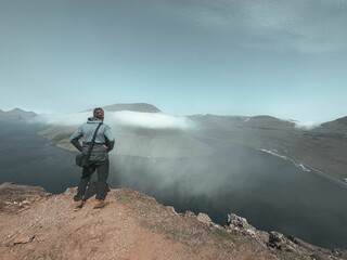 Sticker - Young adult stands atop a rocky cliff, marveling at the breathtaking view of the Faroe Islands