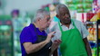 © Marco - Senior diverse employees of grocery store discussing management of business at supermarket aisle wearing uniforms