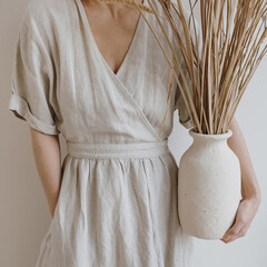 young beautiful woman in neutral beige creamy linen dress holding sandy earthenware with dried pampa