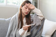© Pormezz - Woman measuring temperature her body on the bed. person got fever lying on the bed.